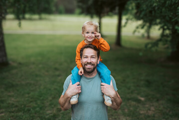Father carrying his smiling son on shoulders during walk in park