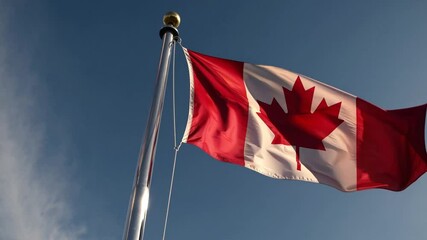 Canadian flag waving on a pole against clear blue sky, symbolizing national pride, patriotism, Canadian identity, sovereignty, independence, and political unity in Canada’s iconic maple leaf emblem