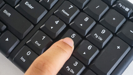 Finger pressing number 5 five button on a black wireless computer keyboard isolated on white...