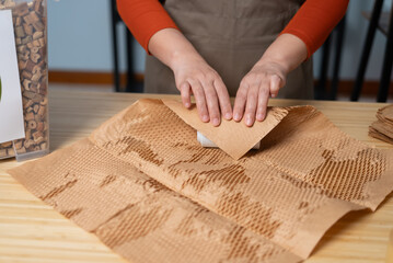 A close-up of a woman’s hands packaging a product using 100% reusable materials, promoting eco-friendly shipping, sustainability, waste reduction, and responsible consumption.