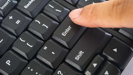 Finger pressing enter button on a black modern wireless computer keyboard isolated on white...