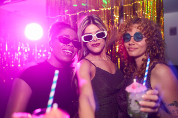 Cheerful diverse women enjoying nightlife, posing at trendy disco party