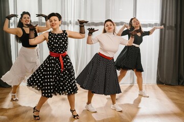 Four pinup women dancing rock and roll or lindy hop wearing polka dots dresses