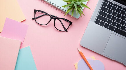 Elegant Workspace with Laptop, Glasses, Plants, and Stationery on Pink Background