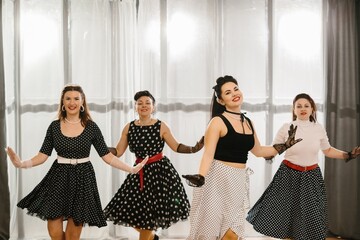 Four pinup dancers wearing fifties style polka dot dresses performing rock and roll dance