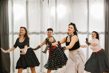 Four pinup dancers wearing polka dots dresses and gloves are dancing swing in studio