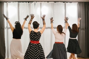 Four pinup dancers raising arms in fifties style dress