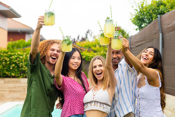 Happy friends raising lemonade glasses at pool party celebrating summer together