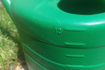 Green watering can with a capacity of 10 liters placed on a sunny garden path surrounded by grass