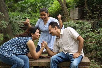 Indian mother and daughter together Arm Wrestle at park. father cheep up Infront to both
