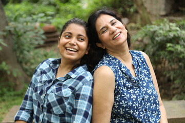 Fototapeta premium Indian happy mother having fun caring, hugging, enjoyment and bonding loving with her daughter. Two indian woman sitting and enjoying at park. 