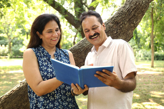 Indian happy mature couple reading story book at park.