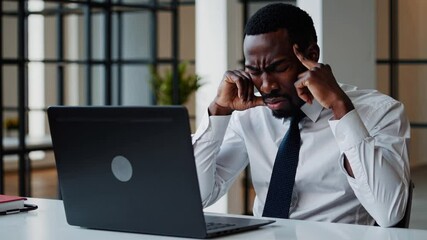 Frustrated African businessman struggling with work stress at office desk, holding head in pain, concept of burnout, mental exhaustion, pressure at workplace, overworked professional under deadline