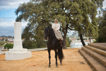 Young horsewoman riding a black Spanish thoroughbred horse, happy riding with him. She has saddle...