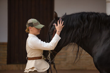 Portrait of young horsewoman caressing her black Spanish thoroughbred horse, with affection and...