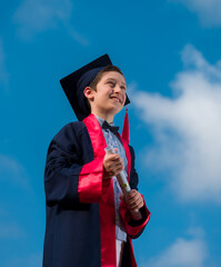 Handsome boy with elementary school graduation outfit and diploma. Boy in graduation robes looking...