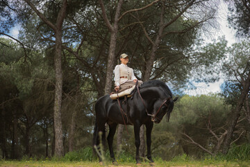 Young horsewoman riding her black Spanish thoroughbred horse, posing in the middle of the field....