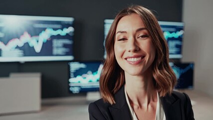 Confident smiling businesswoman in professional attire standing in financial office with digital trading and analytics data displayed on large screens behind her - career success, finance, leadership - Powered by Adobe