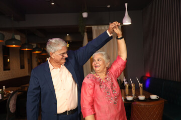 Active seniors spending quality time at cafe. 
Indian happy elderly old senior couple grandparents dancing together at restaurant cafe.