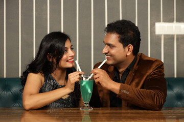 Close-up of young indian couple having mocktail 
in cafeteria