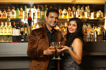 Indian loving couple toasting cocktail and beer glass at bar counter. Couple celebrating anniversary 