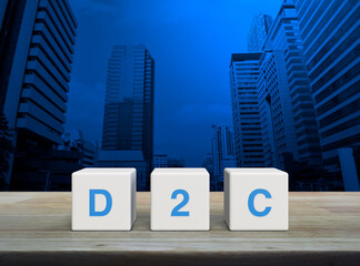 D2C acronym on white block cubes on wooden table over modern office city tower and skyscraper, Direct to Consumer concept