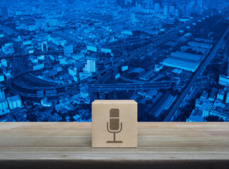 Microphone flat icon on wood block cube on wooden table over modern city tower, street, expressway and skyscraper, Technology communication concept