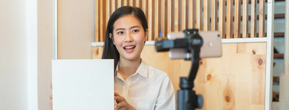 Asian young influencer talk to camera and  review new product. filming video by use mobile phone at home.