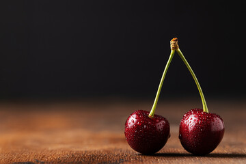 Two juicy cherries or sweet cherries on one branch covered with water droplets. Dark background, old wooden brown table. Space for text. Summer berries and fruits