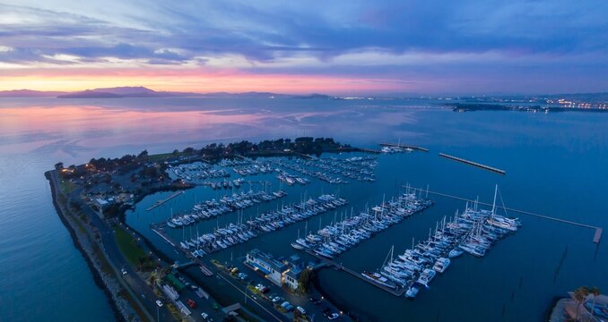 Aerial view of Emeryville Marina filled with sailboats at dusk in the United States. The boats are docked, awaiting their next voyage on the open water. Emeryville, California, USA - Powered by Adobe