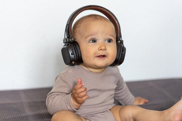 Baby sitting in headphones. Focused expression. Cozy indoor moment