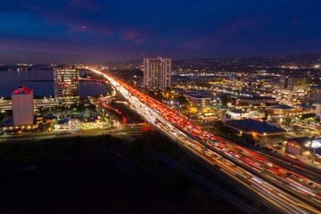 Night aerial view of highway traffic in Emeryville, California, USA. Cars are traveling to their destinations, creating light trails. City lights illuminate the urban landscape.