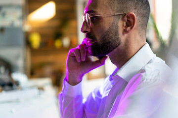 Pink light falling on businessman talking through mobile phone in office