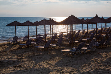 Row of wooden umbrellas at sandy beach, sea during the sunset