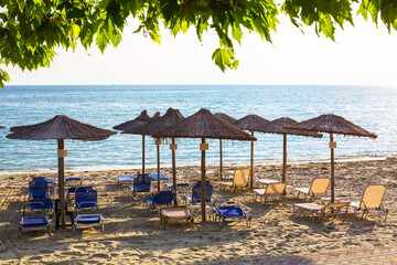 Row of wooden umbrellas at sandy beach, sea during the sunset