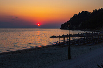 Tropical beach umbrellas, sun and colorful sunset sky