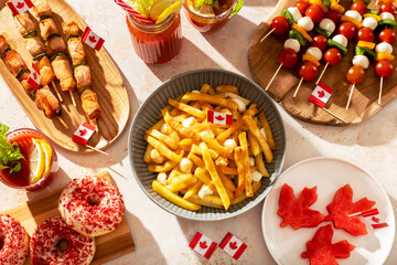 Top view of Canada Day party food with poutine, hot dogs, fruit, skewers, and donuts decorated with...