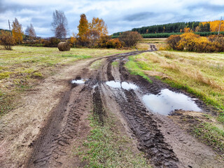 The picturesque rural landscape boasts muddy paths winding through vibrant autumn foliage, all...