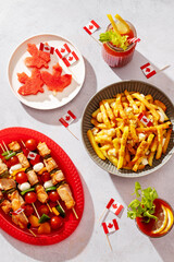 Top view of Canada Day party food with poutine, hot dogs, fruit, skewers, and donuts decorated with Canadian flags