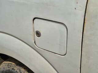 Close-up of a dirty white fuel tank cover on an old vehicle with visible wear and rust