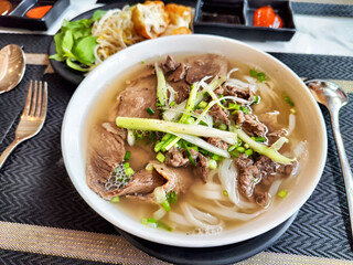 Indulging in a delightful bowl of authentic Vietnamese pho, featuring succulent tender beef and a medley of vibrant, fresh herbs