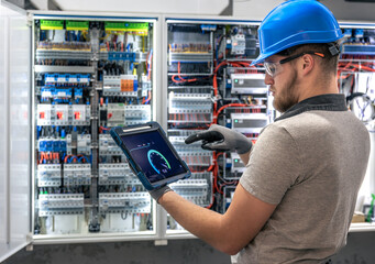 Electrician checks tablet. Digital system control. Work at switchboard.