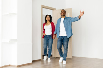 Happy young Black couple entering new home together, holding hands and smiling, dressed casually, african american spouses enjoying a fresh start in bright modern apartment interior