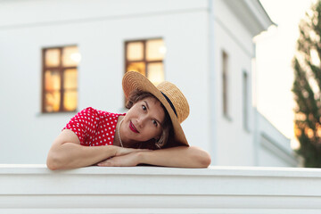Woman in red polka-dot dress rests head on white parapet.