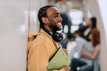 Student smiling while leaning against a wall in a university hallway with classmates in the...