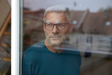 Man with glasses looking out a window in a loft, reflecting a serene and contemplative mood