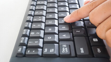 Finger pressing letter D button on a black wireless computer keyboard isolated on white background
