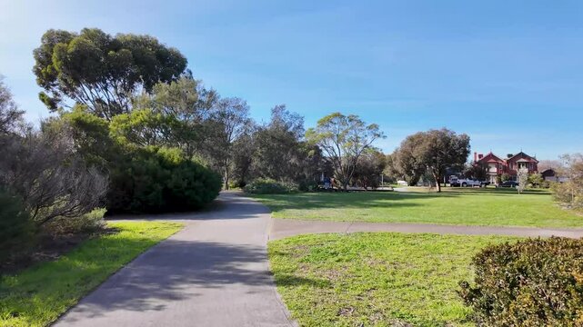 Walking trail or footpath winds through a spacious green park in Williamstown, Melbourne Australia, with open lawn, trees, and suburban homes. Calm and inviting atmosphere for outdoor recreation