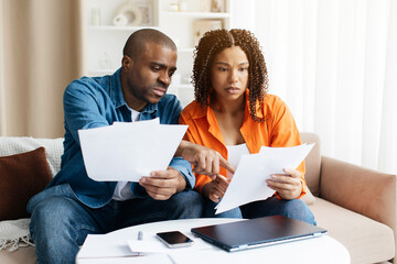 Upset Young Black Couple Suffering Financial Crisis Checking Papers At Home, Millennial African...