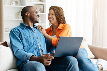 Affectionate moment between young couple at home smiling at each other while sitting on couch with...